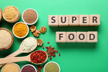 Different superfood products and words made of wooden cubes on green background, flat lay