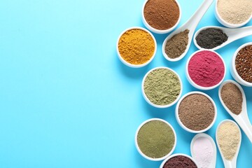 Different superfood powders in bowls and spoons on light blue background, flat lay. Space for text