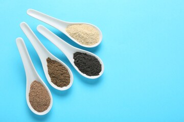 Different superfood powders in spoons on light blue background, flat lay. Space for text