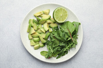 Cut ripe green avocado, greens and lime on light grey table, top view
