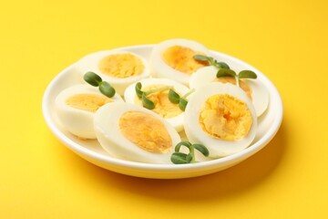 Halves of hard boiled eggs with microgreens on yellow background, closeup