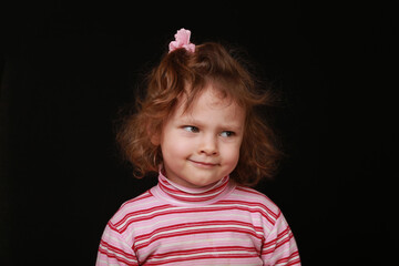 Portrait of baby girl with blond hair with skeptic emotion face. Close Up little expression facial beauty little kid in casual pink clothes. Black studio background