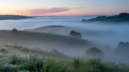 Obraz premium Misty morning landscape depicting rolling hills under a pink and blue sunrise sky