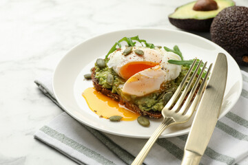 Delicious sandwich with avocado, poached egg, arugula and pumpkin served on table, closeup
