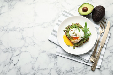 Delicious sandwich with avocado, poached egg, arugula and pumpkin served on white marble table, flat lay. Space for text