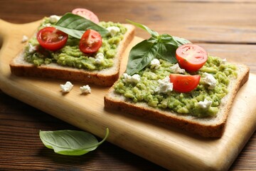 Delicious sandwiches with avocado, tomatoes, basil and cheese on wooden table, closeup