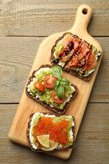 Different delicious avocado sandwiches on wooden table, top view