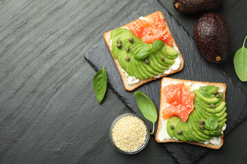 Delicious sandwiches with avocado, salmon, cream cheese, basil and sesame seeds on black textured table, flat lay . Space for text
