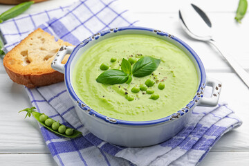 Tasty pea cream soup with basil served on white wooden table, closeup