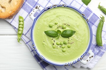 Tasty pea cream soup with basil served on white wooden table, flat lay