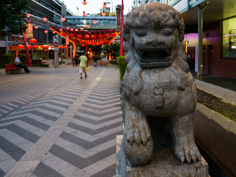 Early evening photo of lion statue in Chinatown with patterned paving and red lanterns