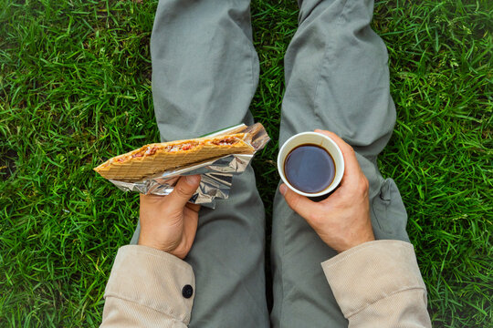 Close-up view of a man sitting on the grass enjoying a oblea and coffee in the park, for the concept of eating out, street food, and relaxation. High quality photo