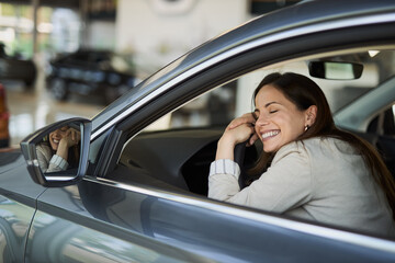 Happy woman enjoying inside of her new car while leaning on steering wheel in a showroom. 