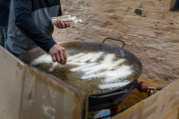 A man prepares churros in a big frying pan full of boiling oil