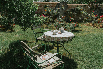 Serenic image of a charming garden with a table set for tea amidst blooming roses and greenery, evoking calmness and leisure