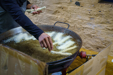 A man prepares churros in a big frying pan full of boiling oil