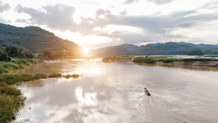 Scenic view of the Mekong River at sunset, with a longtail boat gliding through the golden water. This peaceful river landscape captures nature, simplicity, and freedom.