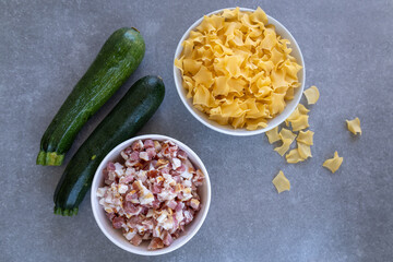 zucchini, pasta and diced bacon in white bowl on grey kitchen counter