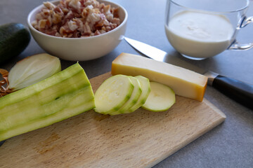 peeled zucchini, diced bacon, cream and cheese on grey kitchen counter side view