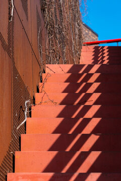 Red stairs with shadows and light patterns, urban geometry and architectural textures, ideal for architecture, design, and city stock photography.