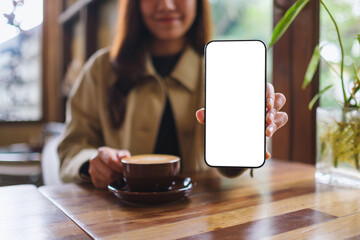 Mockup image of a woman holding and showing mobile phone with blank white screen in cafe