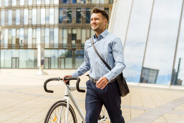 Man in a stylish outfit walks beside his bicycle in a vibrant modern city under a clear sky.