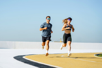 Energetic couple enjoys morning run on bright sunny day along outdoor track with stunning skyline...