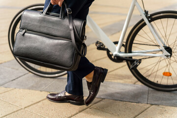Fototapeta premium Gentleman carrying a sleek leather bag while walking alongside a bicycle in a bustling urban area