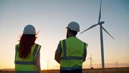 Engineers in safety gear observing wind turbines at a vast wind farm during a beautiful sunset, symbolizing renewable energy and a sustainable future.