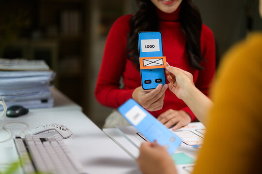 Two web designers testing interactive mobile application prototype on a desk in the office