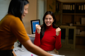 Two businesswomen working together in office, one celebrating success