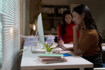 Young professional woman concentrating on her work on desktop computer in modern office at night,...