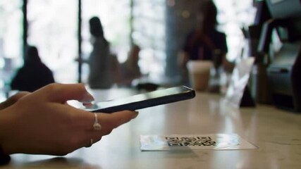 Close-up of hands holding a smartphone scanning a QR code on a counter in a modern cafe, highlighting digital payment or information access. - Powered by Adobe