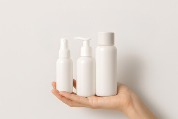 Woman's hand holding different types cosmetic product bottles. Beige tones and modern branding concept. Travel set