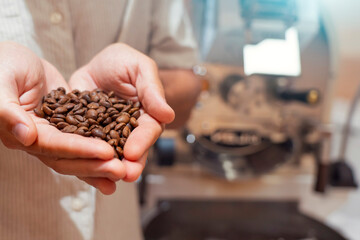 Worker inspects fragrant roasted coffee beans taking them in his hands at production plant close up