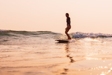 Surfer girl surfing on surfboard on small ocean wave with warm sunrise