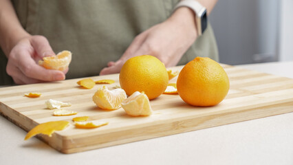 Hands peeling of orange tangerines on the cutting board on table, lots of juicy fresh fruits for cooking on Christmas