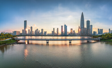 Naklejka premium Panoramic view of modern city skyline with commercial skyscrapers and a bridge over the water at sunset in Shenzhen.