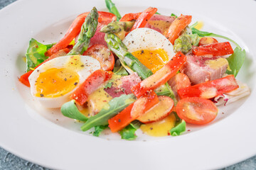 Elegant Niçoise portion with eggs, tuna, arugula, asparagus, cherry tomatoes, white plate
