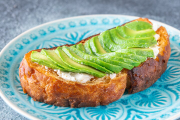 Toasted white bread with labneh spread and avocado slices on blue plate