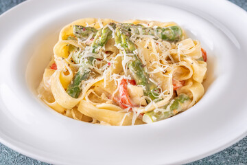 Tagliatelle pasta with creamy garlic sauce, asparagus, peppers, and parmesan topping