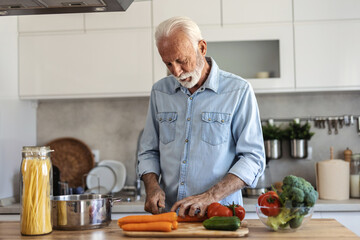 Happy senior man having fun cooking at home - Elderly person preparing health lunch in modern kitchen - Retired lifestyle time and food nutrition concept.
