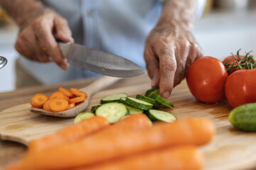 Hands, food and nutrition with a man cooking in the kitchen while cutting vegetables on a wooden chopping board. Salad, health or diet with a chef preparing a meal while standing alone in his home.