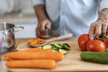 Hands, food and nutrition with a man cooking in the kitchen while cutting vegetables on a wooden chopping board. Salad, health or diet with a chef preparing a meal while standing alone in his home.