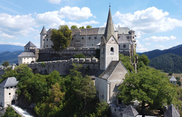 Aerial view of a medieval Hochosterwitz castle and church tower in the Austrian Alps. Stone walls, forest, and mountain landscape. European architecture and cultural heritage. Travel destination. 