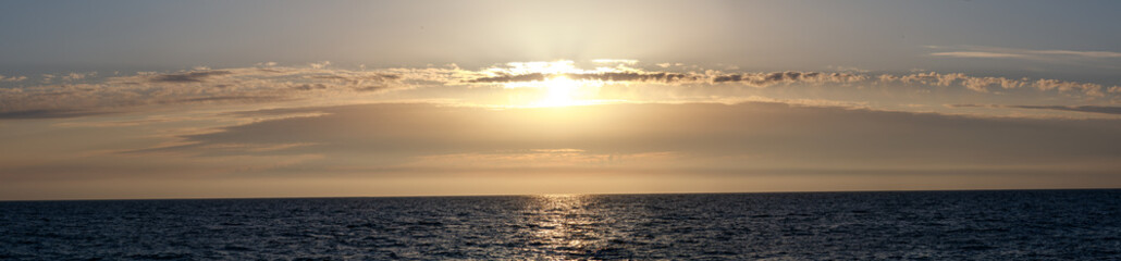 The sun is setting over the ocean, casting a warm glow on the water
