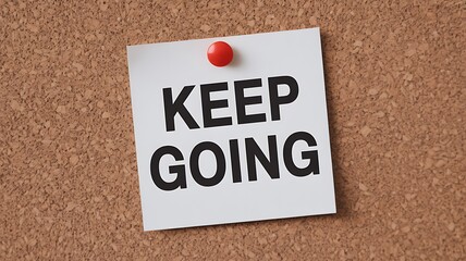A square white note with keep going in black letters pinned to a cork board wall