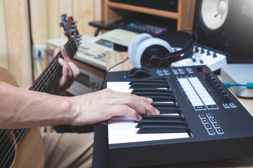 close up male musician hand playing midi keyboard and acoustic guitar for composing a song. song writing, music production concept
