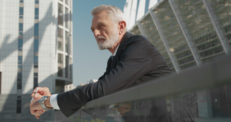 Gray-haired businessman holding cigarette, standing outside, smoking during break