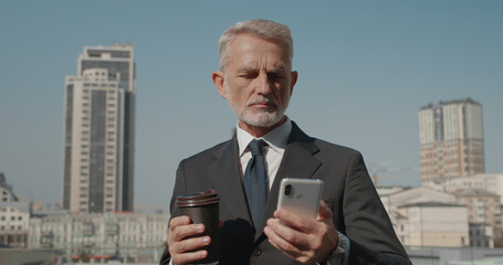 Successful company director holding coffee cup, reading business news on phone
